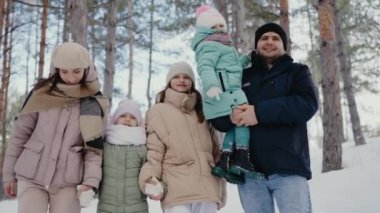 Beş çocuklu neşeli bir aile, aileleri ve üç çocuğu, sıcak giyimli, karla kaplı bir ormanda birlikte, serin kış mevsimini gülümseyerek kutluyorlar. Mutlu Aile Kış Tatili