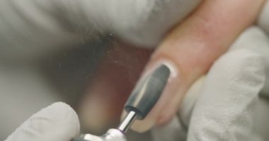 Master manicurist doing manicure procedure for woman client in beauty salon, remove gel polish with electric nail machine and clean finger using brush. A manicurist works with a milling machine. Macro