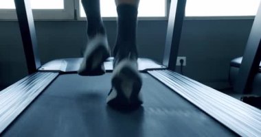 Spor salonundaki koşu bandında koşan bir sporcunun ayak hareketleri, spor ortamında hız ve dayanıklılığı vurguluyor. Modern Spor Salonu 'nda Koşu bandında Koşan Sporcu