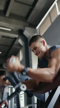 Sporcu, modern bir spor salonundaki egzersiz makinesinde yoğun bir şekilde çalışıyor. Güç ve kararlılık gösteriyor. Dikey Jimnastik Salonunda Egzersiz Makinesi Üzerinde Çalışan Odaklanmış Sporcu