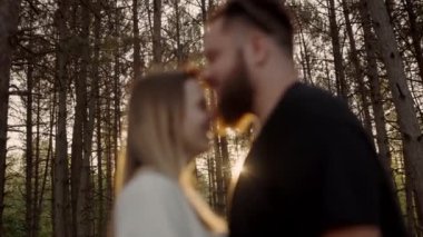 Ormanla çevrili bir çiftin öpüştüğü samimi bir an. Batan güneş, romantik atmosferi güçlendirmek için sıcak bir parıltı ekliyor. Günbatımında Ormanda Öpüşen Romantik Çift