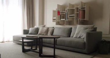 Rahat, gri bir kanepe, şık duvar rafları ve doğal ışıklandırması olan modern bir oturma odası. Minimalist tasarım ve rahat mobilyalar davetkar ve huzurlu bir atmosfer yaratıyor..