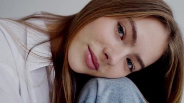 Yüksek çözünürlüklü görüntü, koluna yaslanmış çarpıcı gözlerle genç bir kadının huzurlu ifadesini yakalıyor. Güzellik, tefekkür ve gençlik teması için mükemmel. Genç bir kadının yakın plan portresi.