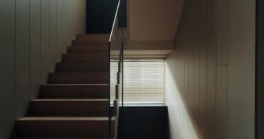 Çevredeki Güneş Işığı ve Minimalist İç mekânlı Modern Tahta Merdiven. Ahşap basamakları ve minimalist dizaynı olan şık, modern bir merdiven. Perdelerin arasından hafif güneş ışığıyla aydınlatılıyor..