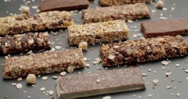 Gri bir yüzeye yerleştirilmiş çeşitli besleyici granola çubukları. Görüntüde farklı tat ve dokular, dağınık yulaf ve fındıklar yer alıyor. Sağlıklı beslenme kavramları için mükemmel..