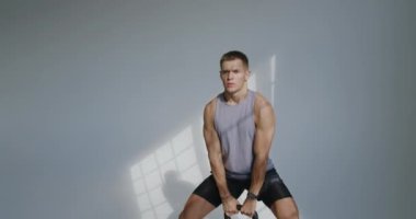 Atletik Genç Adam Stüdyoda Kettlebell Eğitimine Başladı. 23 yaşında atletik bir adam modern bir stüdyoda bir su ısıtıcısıyla çalışıyor. Gücünü ve dikkatini gösteriyor..