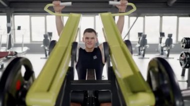 Genç yetişkin bir erkek, iyi donanımlı bir fitness merkezinde ağırlık antrenmanı yaparken yoğun bir şekilde konsantre oluyor. Gücünü ve bağlılığını gösteriyor. Odaklanmış Genç Adam Spor Salonunda Sıkı Çalışıyor