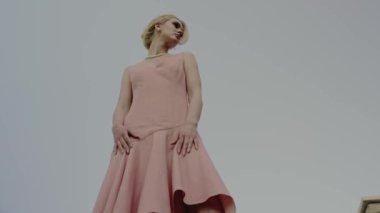Kendine güvenen, şık pembe elbiseli ve inci kolyeli, açık havada, gökyüzüne karşı poz veren bir kadının düşük açılı görüntüsü. İnci Kolyeli Pembe Elbiseli Kendine Güvenen Kadın Açık havada