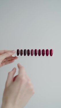 Manikür salonundaki bir paletten oje rengini seçen bir elin yakın çekimi. Çeşitli kırmızı ve kestane renkleri sergilenmektedir. Manikür Seçimi İçin Tırnak Cilalı Renk Örnekleri Tutan Kadın