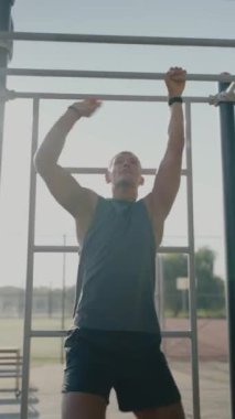 Genç bir sporcu, güneşli bir günde güç ve dayanıklılık odaklı açık hava fitness parkında maymun parmaklıkları üzerinde egzersiz yapıyor. Açık Spor Parkı 'nda Maymun Barları Eğitiminde