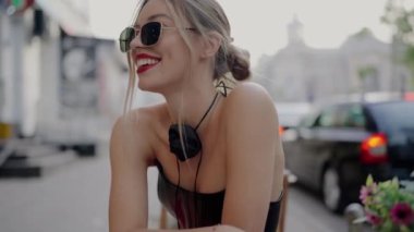 Kendine güvenen, şık güneş gözlüğü takan ve kırmızı ruj süren genç bir kadın, açık hava ortamının tadını çıkarıyor. Kırmızı rujlu ve güneş gözlüklü şık genç bir kadın.