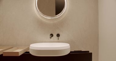 Modern minimalist banyo, parlak beyaz bir lavabonun üzerinde şık, dairesel bir ayna sergiliyor. Tarafsız tonlar ve temiz çizgiler sakin bir atmosferi çağrıştırıyor. Modern Minimalist Banyo