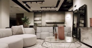 Modern contemporary Minimalist living room with white and beige furniture and white kitchen room. Luxury Modern House Interior With Corner Sofa, Chairs and Bookshelf. Fashionable furniture.