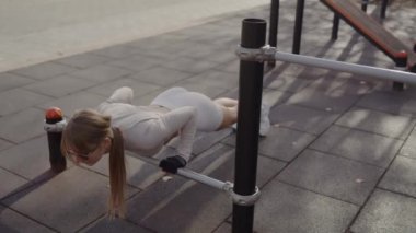 Güneş Gözlüklü Genç Kadın Açık Hava Spor Salonu 'nda. Güneş gözlüklü ve spor giysili odaklanmış genç bir kadın spor kıyafetlerini spor amaçlı kullanıyor. Açık hava spor aletlerini kullanıyor..