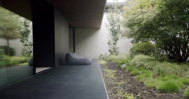 Şık ve çağdaş ev terasında rahat bir armut koltuk, cam kapılar ve gür, manikürlü bir bahçe manzarası var. Moda Fasulye Torbası ve Lush Garden Manzaralı Modern Ev Terası