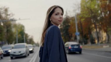Şık, koyu renk ceketli düşünceli genç bir kadın, işlek bir şehir caddesinde sonbahar ağaçlarıyla yürürken derin derin düşünüyor. Kentsel yaşamın ve bireysel düşüncelerin mükemmel tasviri.