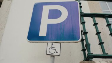 Duvara asılmış mor bir P engelli park levhasının yakın çekimi Portekiz 'in bir kentindeki engelliler için ayrılmış bir park yeri olduğunu gösteriyor. Otopark için mavi yol tabelasına yakın çekim