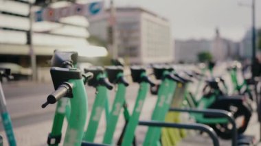 Güneşli bir günde kentsel bir ortamda park etmiş bir dizi yeşil elektrikli scooterın yakın plan görüntüsü, çevre dostu ulaşım ve şehir içi ulaşım eğilimlerini vurguluyor.