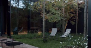 Modern evlerin dış görünüşü, gösterişli, gösterişli bir tasarım ve rahat koltukları olan davetkar bir bahçe. Zarif Bahçeli ve Rahatlatıcı Sandalyeli Modern Ev Dışı