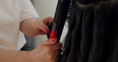 Female hairdresser making haircut to young client using curling iron in beauty studio. Handheld view of hairstylist creating trendy hairstyle. Creating hairstyles hairdresser at salon. indoor shot