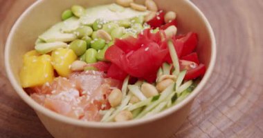 Poke kasesi, geleneksel Hawaii çiğ balık salatası. Somon, pirinç, avokado, edamame fasulyesi, ahşap zemin üzerinde salatalık. Sağlıklı yemek, keto diyeti konsepti. Asya çiğ yemeği.