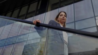 Genç profesyonel bir kadın, arka planda yansıtıcı modern ofis binası bulunan bir yürüyen merdivenden iner. Şehir yaşamını ve kariyer hırsını yakalamak.