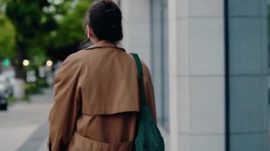 Şehir ortamında yürüyen sakin yüzlü genç bir kadın. Günlük bir ceket ve beyaz gömlek giyiyor. Sıradan bir gezintiye ya da işe gitmeye benziyor. Şehir sokağında şık giyimli bir kadın.