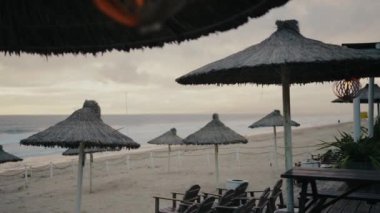 Portekiz 'de gün batımında sakin bir sahil sahnesi. Saman şemsiyeler, sandalyeler ve sakin bir kıyı şeridi. Rahatlama ve sükunet için mükemmel bir tatil yeri görüntüsü. saman şemsiyeleri,