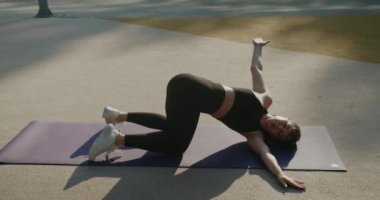 Antrenör şehir spor sahasında aktif bir sabah geçiriyor. Sağlıklı yaşam konsepti. Yoga egzersizi yapan çekici bir kız. Genç bayan parkda yoga yapıyor..