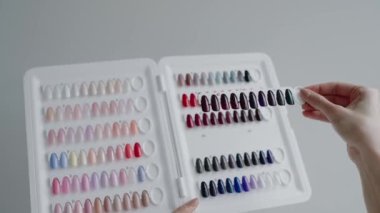 Tırnak cilası renginden çeşitli paletler seçen bir kişi, bir manikür salonu ortamında değişik tonlarda canlı ve pastel renkler sergiliyor. Bir Paletten Tırnak Cilalama Rengi Seçen Kadın