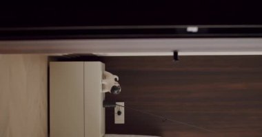 Ahşap bir duvar, minimalist bir başucu masası ve zarif ve gösterişli bir ev dekorasyonu olan modern bir masa lambası içeren çağdaş bir iç mekanın yukarıdan aşağı görüntüsü. Modern İç Tasarım. Dikey