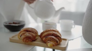 Aydınlık bir sabahta çay ve kahveyle servis edilen tepside iki taze kruvasan. Mükemmel kahvaltı düzeni. Lezzetli Taze kruvasanlar ve Parlak Bir Sabahta Kahvaltı İçin Çay ve Kahve