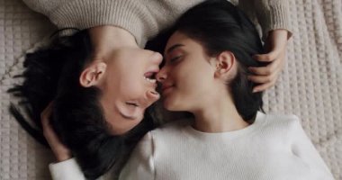 Evdeki aydınlık oturma odasının penceresinde kanepede otururken gülümseyen ve nazikçe el ele tutuşan genç lezbiyen çiftin el kamerası. Sevgi ve desteği paylaşan iki kadın el ele tutuşuyor.