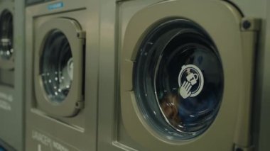 Modern bir çamaşırhanedeki çamaşır makinelerinin detaylı görüntüsü. Temiz, verimli ve ticari yıkamaya dikkat edin. Çamaşır Odasında Çamaşır Makinesinin İçi Giysilerle Kapalı