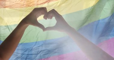 Gay and lesbian pride lgbt flag. Supporting hands make heart sign and wave in front of a rainbow flag flying. Love sign. Celebration Event Symbol Of LGBT. Love Equal. LGBT rights. human relationships.