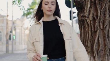 Gündelik giysiler içindeki kendine güvenen genç bir kadın güneşli bir günde arka planda ağaçlar ve bir binayla dışarıda yürüyor. Güneşli bir günde açık havada yürüyen kendinden emin genç bir kadın.