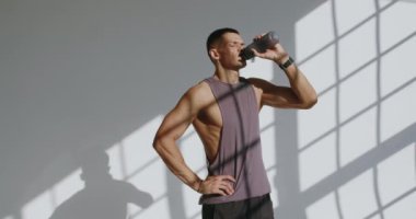 23 yaşında atletik fiziği olan, yorucu bir stüdyo çalışması sırasında suyunu yudumlayan bir adam. Gölgeler ve ışık karşıtlığı sahneyi güçlendirir.