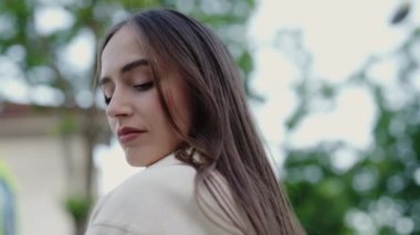 Sakin bir ifadeyle omzunun üstünden bakan genç bir kadının yakın plan portresi. Yeşil doğa geçmişi. Arka planda Yeşil Yapraklı Serene Genç Kadın