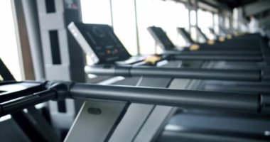 Modern bir spor salonunun gösterişli manzarası, geniş, doğal ışıklandırılmış bir odada düzenli sıralanmış ileri koşu bantları. İyi-Aydınlatma Alanındaki Koşu Değirmenleri Sıraları ile Modern Spor Salonu