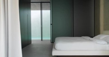 Parlak minimalist tasarımı, beyaz yatak örtüsü ve açık renkli perdenin yanındaki koyu renkli duvarların olduğu sakin, modern bir yatak odası. Zarif Minimalist Tasarımlı Modern Yatak Odası İçi