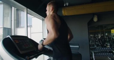 Sağlığını ve dayanıklılığını vurgulayarak, iyi donanımlı bir fitness merkezinde büyük pencerelere bakan, koşu bandında egzersiz yapan kararlı bir adam. Modern bir spor salonundaki koşu bandında koşan odaklı bir sporcu