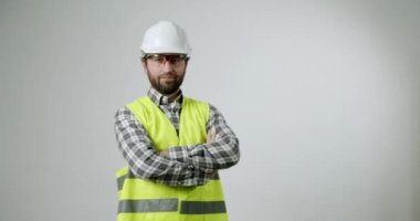 Kendine güvenen inşaat işçisi kolları bağlı duruyor. Sıkı bir şapka, güvenlik gözlüğü ve yüksek görüş mesafesi olan bir yelek giyiyor. Endüstriyel işlerde profesyonellik ve güvenlik bilinci yayar.