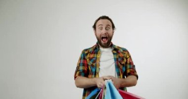 Heyecanlı adam alışveriş torbalarını tutuyor ve sevinçten havalara uçuyor. Satın alımları onu şaşırttı. Perakende satış ve tüketim temaları için harika. Reklamlar, sosyal medya ve web siteleri için mükemmel.