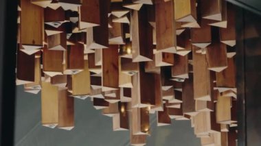 Tavandan sarkan gömülü ışıkları olan tahta üçgen prizmalar. Bu modern sanat eseri her yere zarif bir dokunuş katıyor. Sıcak tonlar ve geometrik şekiller görsel bir cazibe yaratıyor.