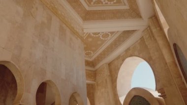 Kazablanka, Fas 'taki Hassan II Camii' nin içindeki bej duvarlar ve süslü tavan. Kemerlere ve detaylı tavana bakarken, karmaşık desenler ve altın süslemeler, ihtişam hissi uyandırıyor.