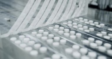 İlaç fabrikasının atölyesinde metal otomatikler üzerinde hareket eden beyaz haplar. Fabrika ekipmanı ve makine taşıyıcısı. Endüstriyel eczacılık konsepti. Uyuşturucuların görünümü taşıyıcı bant boyunca ilerler.