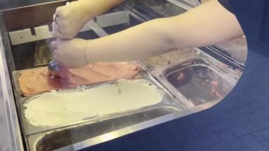 Dondurmacıda sergilenen bir vitrinden dondurmayı kepçeleyen ve çeşitli tatlar sunan ellerin yakın çekimi. Dondurmacıda taze dondurmayı bir koniye kakalamak.