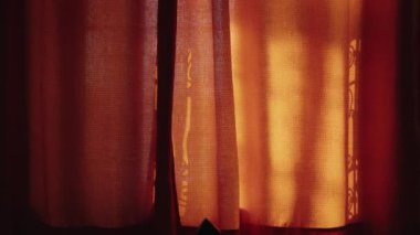 Altın güneş ışığı dokulu kırmızı bir perde boyunca akar ve karmaşık gölgeler bırakır. Sıcak ışık rahat ve davetkar bir atmosfer yaratıyor. Huzurlu bir sabahın özünü yakalamak için mükemmel.