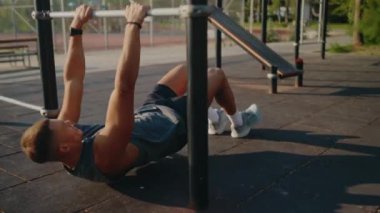 Genç bir adam barfiks çubuğu kullanarak dışarıda egzersiz yapıyor. Sahne, güneşli bir açık havada zindelik, güç ve adanmışlığın özünü yakalıyor. Genç adam dışarıda egzersiz yapıyor.