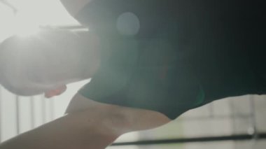 Bir erkek sporcunun kalas egzersizi yaparken gösterdiği yoğun odaklanma ve kararlılığı gösteren yakın çekim görüntüsü. İfadesi ve spor salonu çevresi fitness bağlılığını vurguluyor. Dikey video.